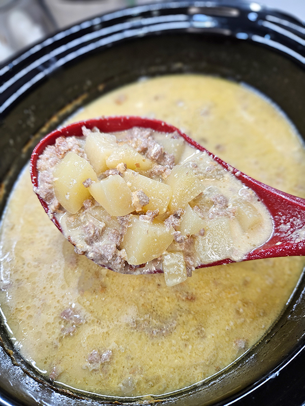 A spoon liting the soup up from the slow cooker.
