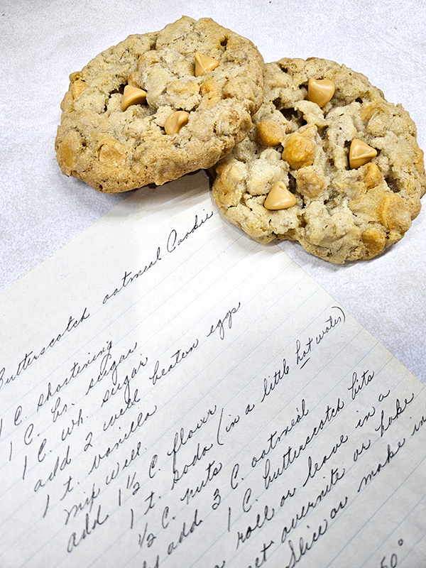 The handwritten recipe with two freshly baked butterscotch oatmeal cookies.