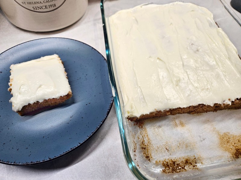 A slice of shortcut carrot bars with cream cheese frosting and the pan.