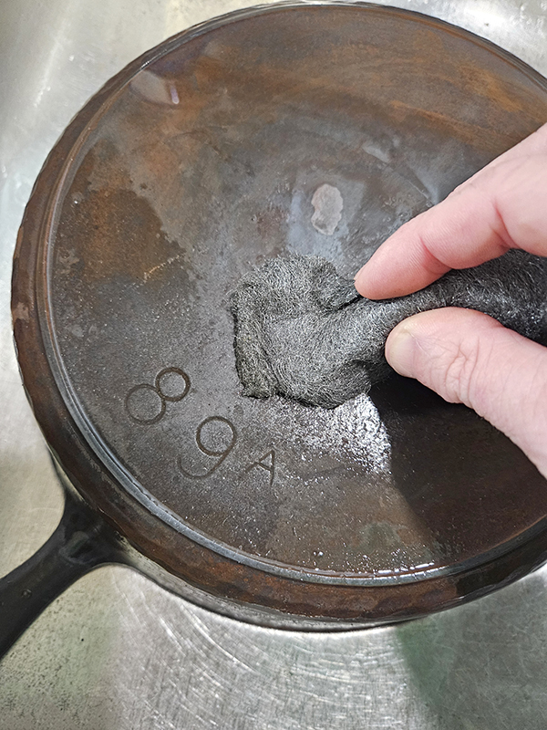 steel wool being used on a rusty cast iron skillet