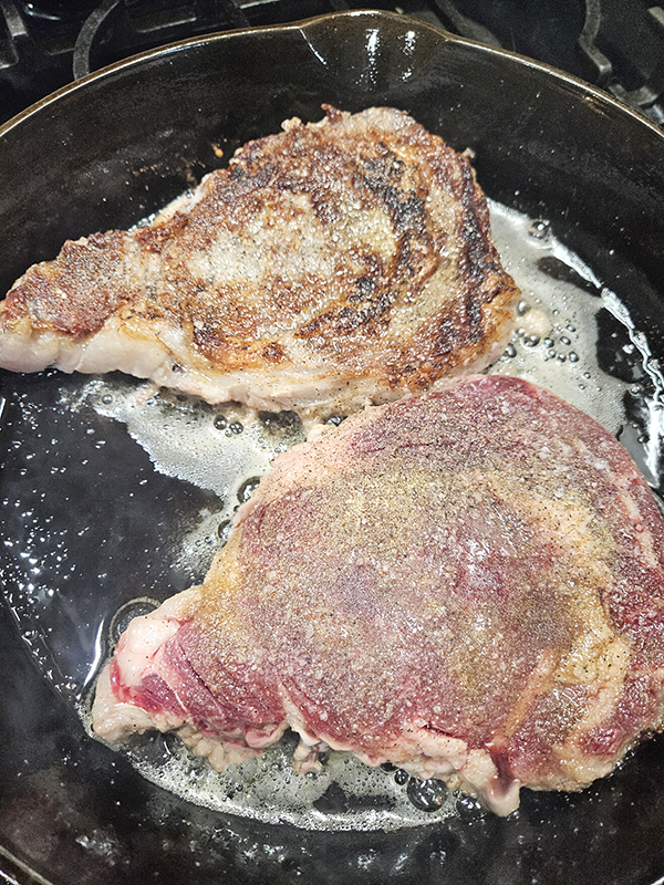 Two steaks in a cast iron pan, one turned and one with a nice sear