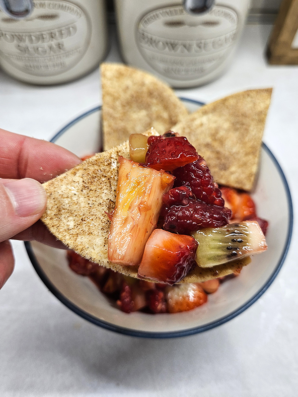 A hand holding a cinnamon sugar chip loaded with fruit salsa