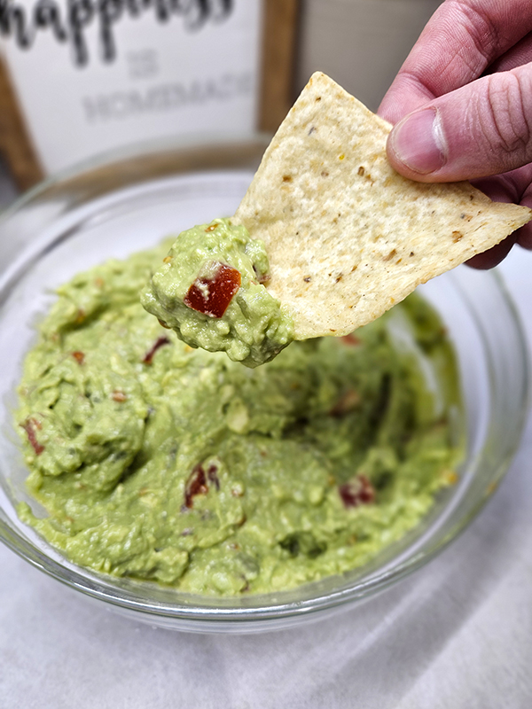 Six ingredient guacamole one a chip with the bowl in the background