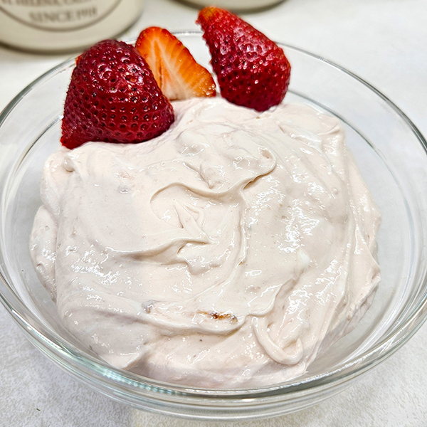 marshmallow strawberry fruit dip in a clear bowl with a couple of strawberries