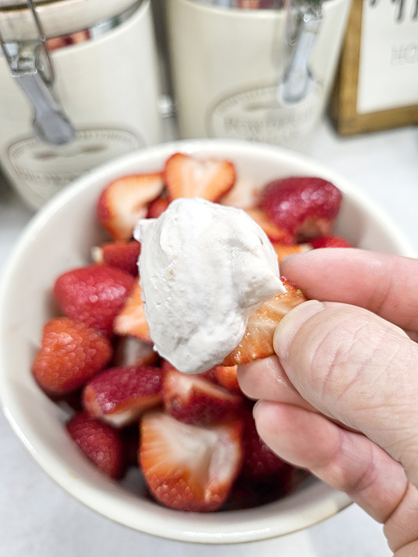 Fingers holding a half of a strawberry with marshmallow strawberry fruit dip on it.