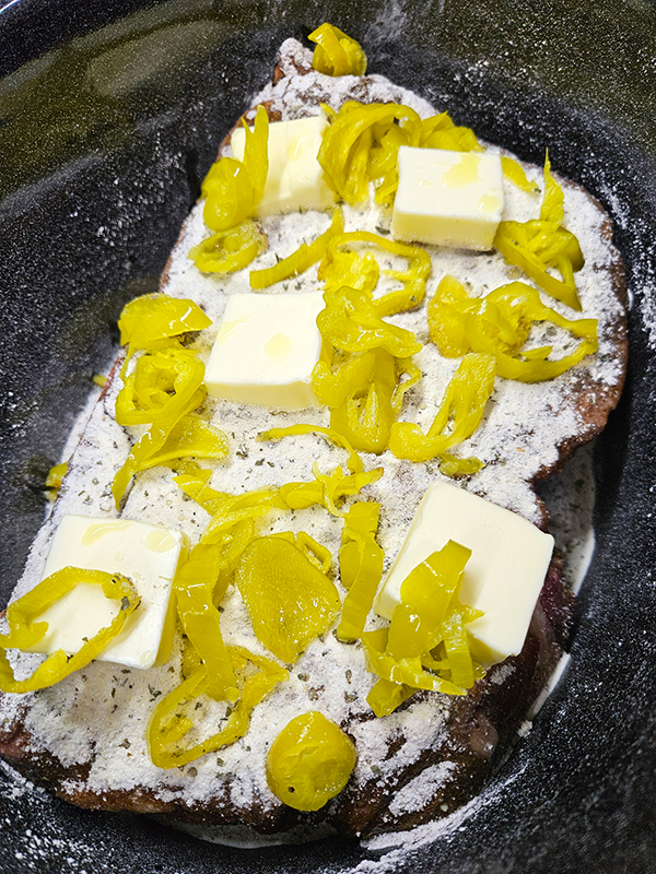 The roast topped with the seasoning, butter, and sliced peppers