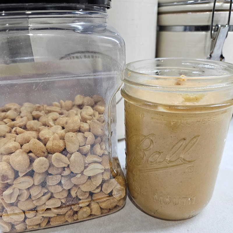 A container of whole peanuts next to a jar of homemade peanut butter