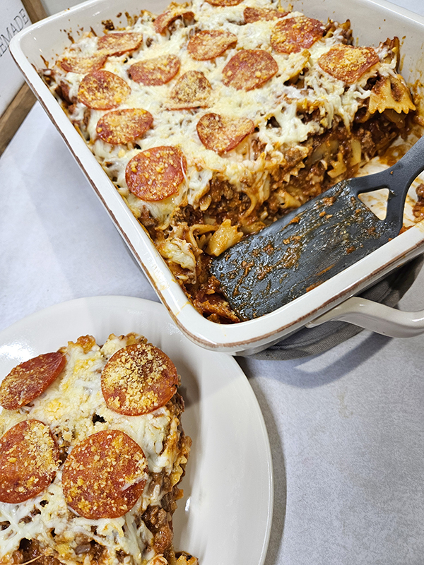 A casserole of pepperoni pizza casserole and one piece cut out on a plate.