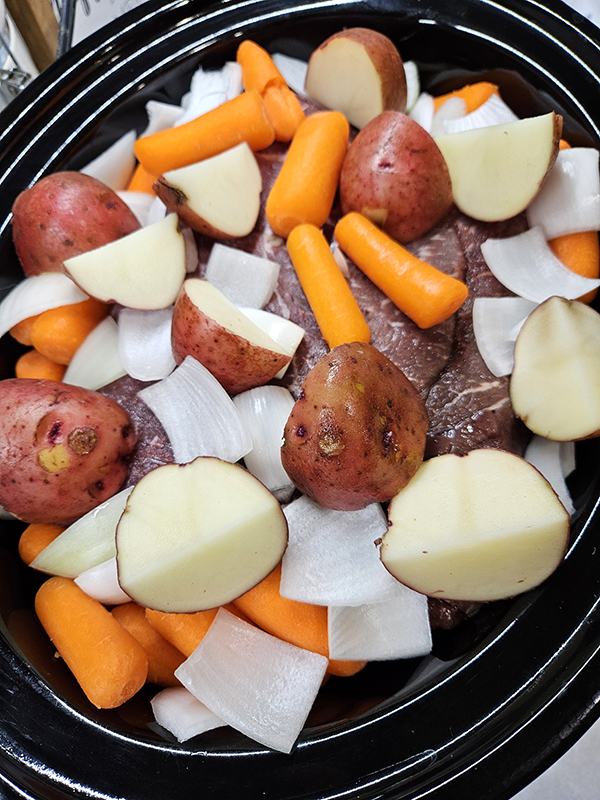A full slow cooker with vegetables and a bit of meat showing