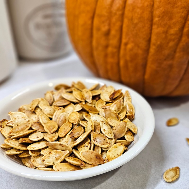 a bowl of Easy Roasted Pumpkin Seeds in front of a pumpkin