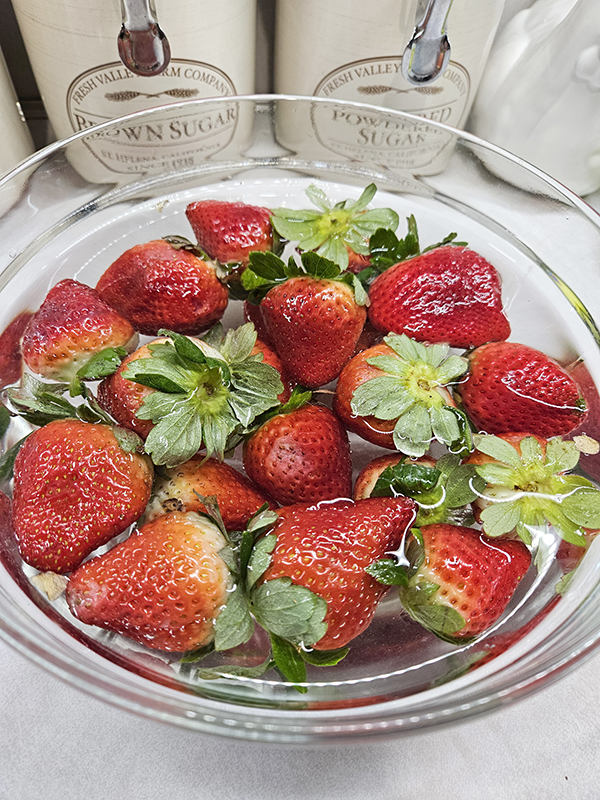 A bowl of strawberries being soaked in a solution of water and vinegar
