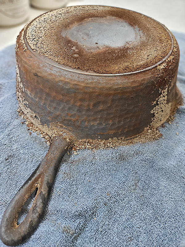 Dried food and seasoning being wiped off of a hammered cast iron pan.
