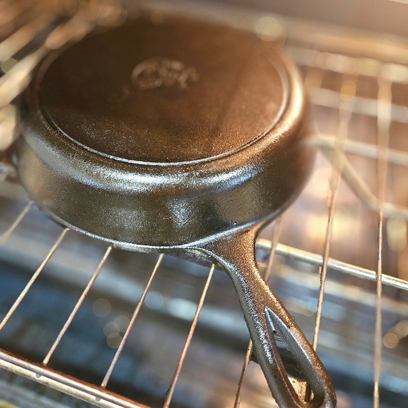 A cast iron skillet getting seasoned in an oven.
