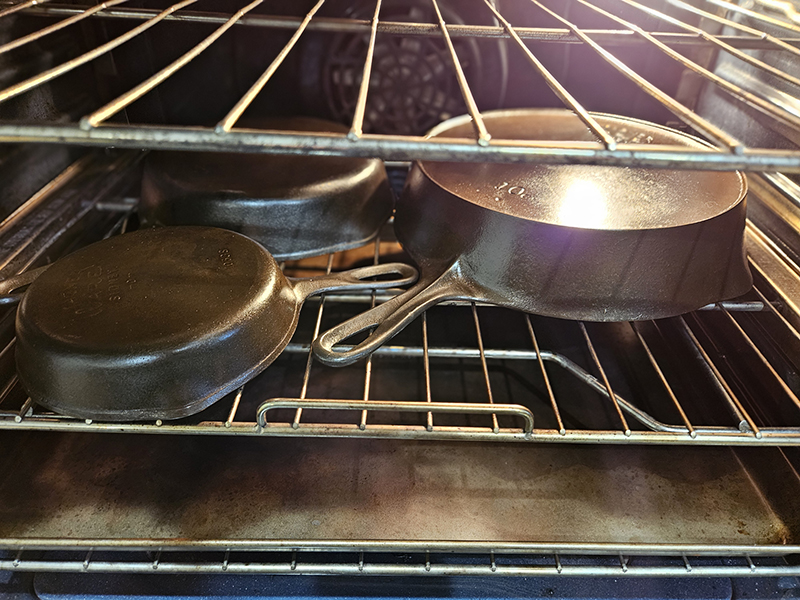 3 cast iron skillets in an oven ready for seasoning and reseasoning