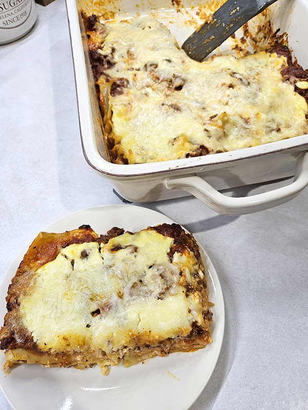 A placed slice of lasagna with the casserole dish behind it. 