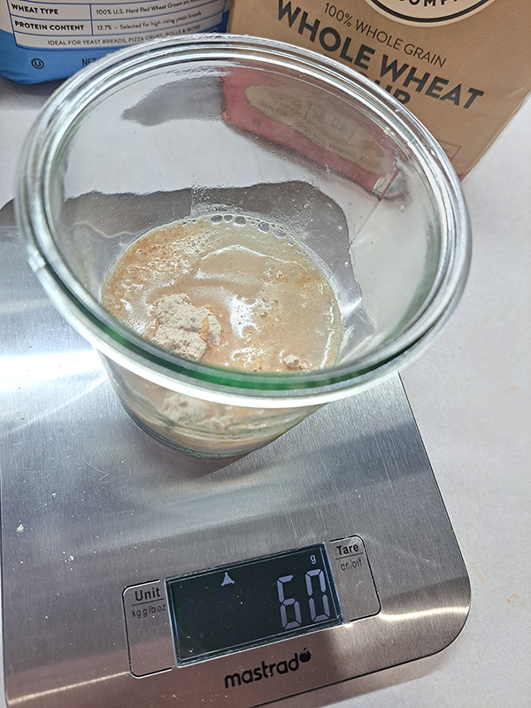 Flour and water inside of a jar that is sitting on a digital kitchen scale