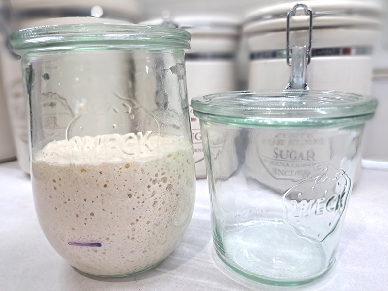 Two different glass jars next to one another, one with active sourdough starter inside and one empty.