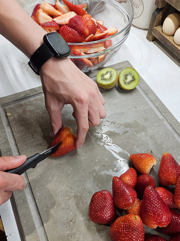 Hands cutting up strawberries.
