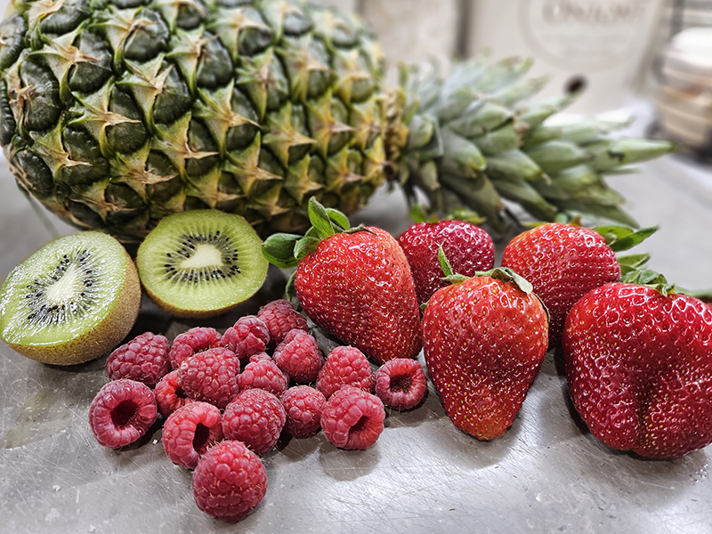 Pineapple, kiwi, strawberries, and raspberries on a gray cutting board.