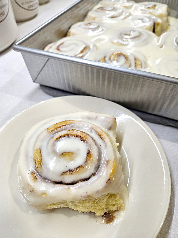 A plate of cinnamon rolls and a baking pan full of them.