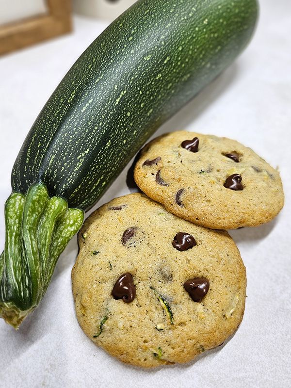 Two chocolate chip cookies next to a whole zucchini